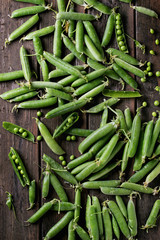 Young organic green pea pods and peas over old dark wooden planks background. Top view with space. Harvest, healthy eating.