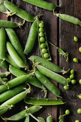 Young organic green pea pods and peas over old dark wooden planks background. Top view with space. Harvest, healthy eating.