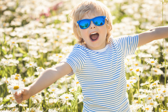 Emotional kid in the camomile field. Cheerful child with flowers wearing hat and sunglasses. Happy boy in the summer time outdoors