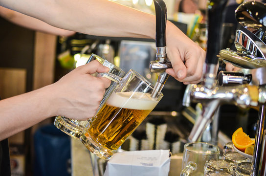 Bartender pouring fresh beer in beer mugs at pub