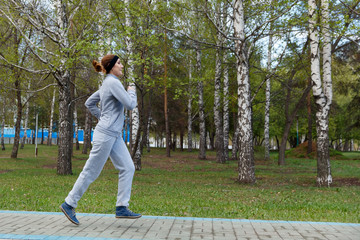 Woman runner running in park. Beautiful sporty fitness model during outdoor workout.