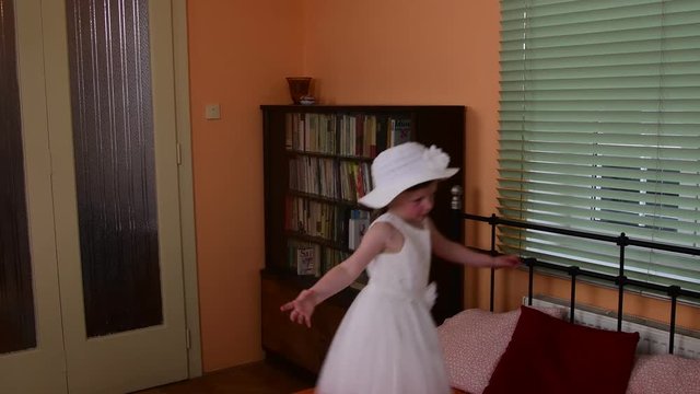 A cute small girl jumping on the bed. Parents bedroom and  her daughter is jumping on the bed.  A small girl is wearing white dress.