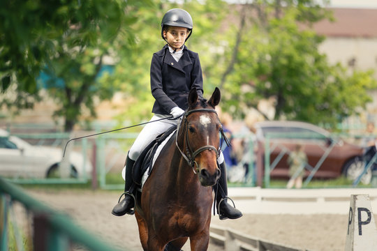 Young teenage girl in helmet riding horse on dressage equestrian competition