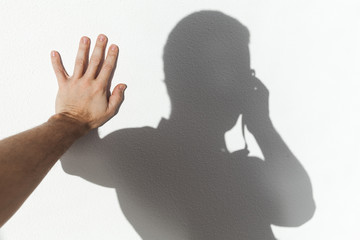 Man touching his shadow on white wall