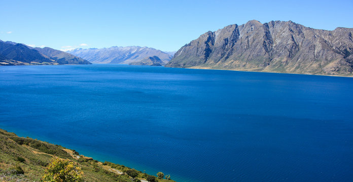 very blue lake with tall lakeside hills in the horizon © Jonas