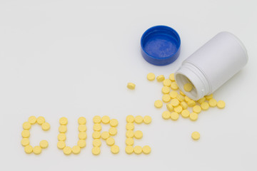 Yellow pills spill put of the bottle and arranged in the word Cure.