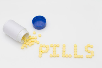 Yellow pills spill put of the bottle and arranged in the word Pills.