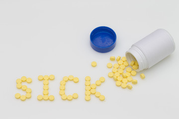 Yellow pills spill put of the bottle and arranged in the word Sick