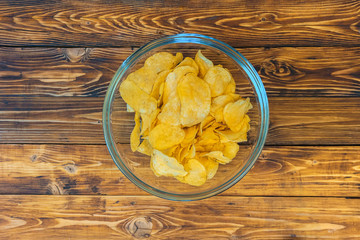 Glass bowl with crisps on wooden table, top view