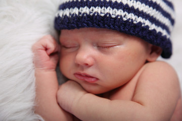 newborn sleeping with hat on fuzzy white blanket