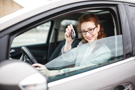 Car rental concept. Woman sitting in car and showing the keys.	