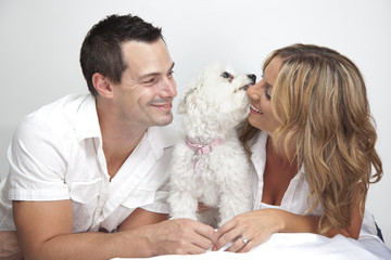 Obraz premium Happy couple with young pet dog, puppy kissing woman.