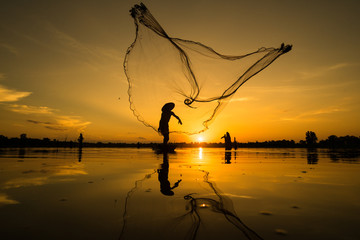 Silhouette of Fisherman catching fish in lake by using fishing net at beautiful sunset time.