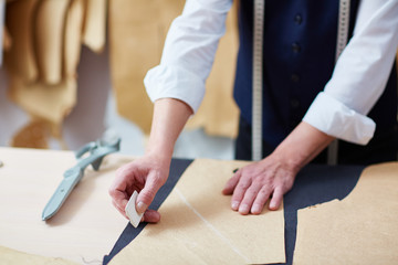 Portrait of unrecognizable skilled tailor working in atelier: tracing patterns on fabric with chalk