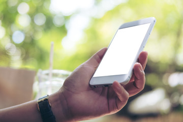 Mockup image of a woman holding and using white smart phone with blank screen at outdoor and green nature background