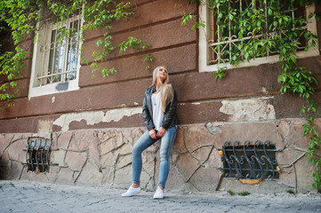 Stylish blonde woman wear at jeans and jacket posed at street against wall. Fashion urban model portrait.