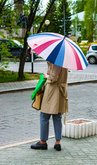Urban street landscape, woman with colorful umbrella standing on the sidewalk