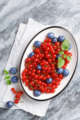 Blueberries and currants in a bowl. Fresh fruits on marble texture. Top view.