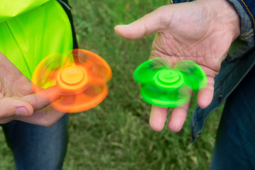 trendy fidget spinner - two persons holding spinning green and orange fidget spinners in hands, close up view