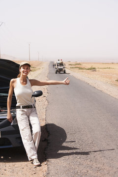 femme souriante en panne de voiture au milieu du désert faisant de l'auto stop