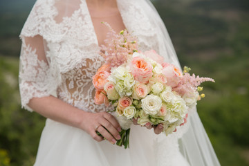 A beautiful wedding bouquet of roses and peonies in the hands of the bride.