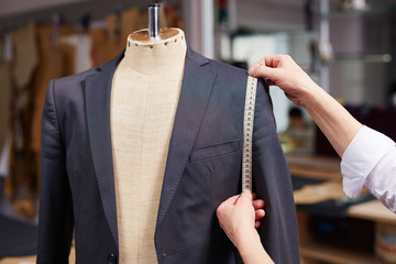 Closeup of tailors hands measuring jacket with tape fitting bespoke suit