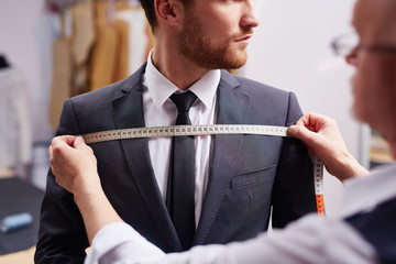 Mid section portrait of tailor fitting bespoke suit to model - obrazy, fototapety, plakaty