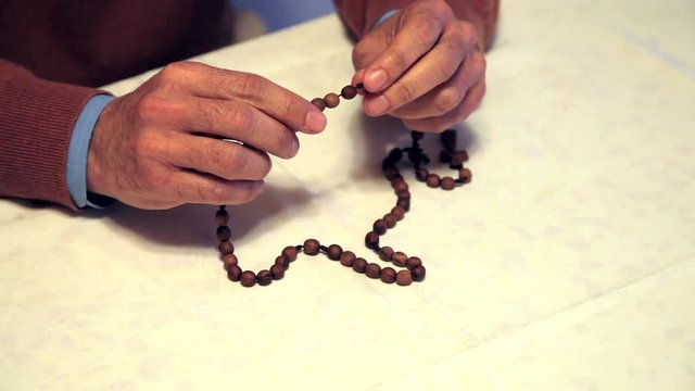 hands of man praying with Rosary beads