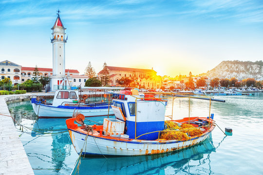 Zante - Zakinthos island, old port with moored boats and church tower landmark. Majestic sunset scenery, sun glowing visible.
