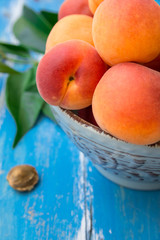 Naklejka na ściany i meble Fresh ripe organic whole apricots in ceramic bowl on blue wood garden table, kernel, green leaves, close up
