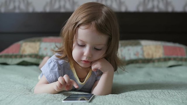 Little girl is looking at the phone. The child is playing on the smartphone. Slow motion