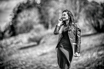 Gadget woman. Portrait of young pretty white girl with black hair and in black clothes talking on the mobile phone and holding a tablet in the hand. Black and white photo. Lifestyle.
