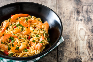 Noodles and shrimps with vegetables in black bowl on wooden table
