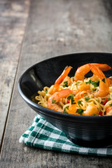 Noodles and shrimps with vegetables in black bowl on wooden table
