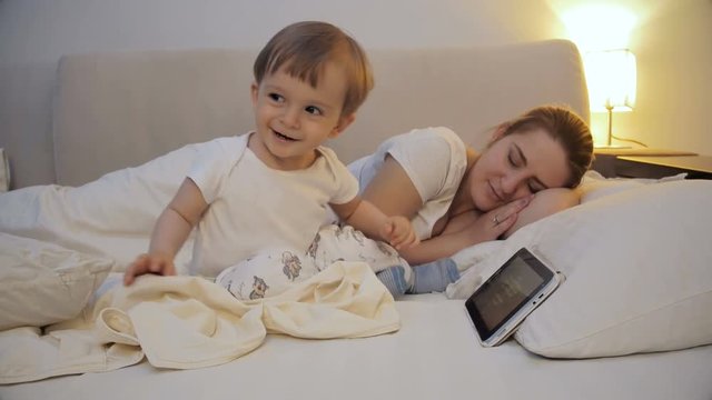 Cute sleepless toddle boy watching cartoons on tablet instead of going to sleep