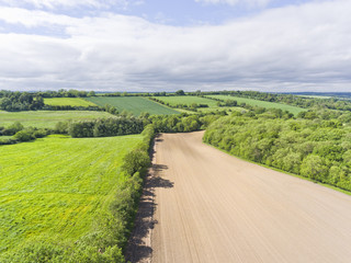 Aerial view of farmed land with ploughed field, green pasture, wheat fields, on an edge of a small woodland, in an English countryside .