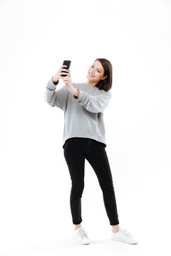 Smiling pretty girl standing and taking selfie on mobile phone