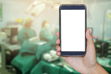 Man hand holding mobile smart phone , tablet,cellphone over Blur of Surgeons team working with Monitoring of patient in surgical operating room background..success with operating room, medical concept