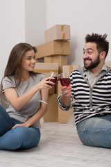 Smiling man and woman drinking wine to celebrate buying new home. Couple on the floor are happily celebrating relocation to new apartment.