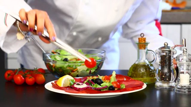 Professional cook prepares a plate with salami and fresh salad