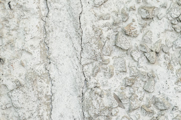 Old white concrete wall with many protruding stones