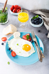 Fried egg on blue plate, tomatoes, blueberries, mint tea and orange juice. Healthy breakfast concept.