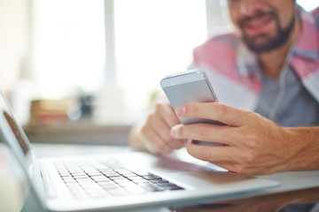 Close-up of businessman checking message on phone while using laptop at desk