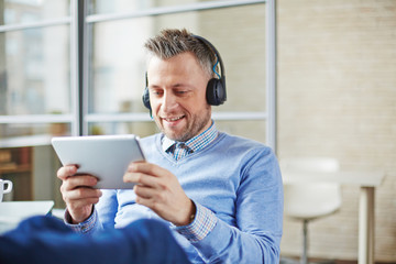 Smiling middle-aged businessman in headphones enjoying webinar when he working in office