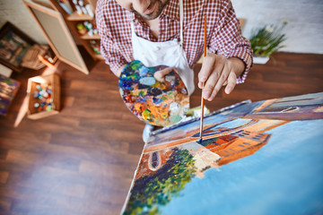 High angle portrait of unrecognizable talented artist painting picture on easel in workshop