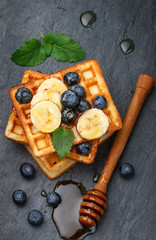 Traditional Belgian waffles with blueberries, banana and honey on a black slate plate. Gourmet Breakfast. Selective focus