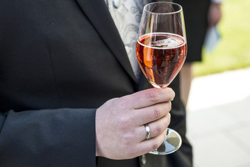 Groom holding glass sparkling wine wedding red champagne suit closeup ring