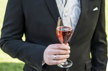 Groom holding glass sparkling wine wedding red champagne suit closeup ring
