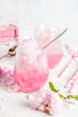 Summer refreshing desserts. Vegan diet food. Ice cream frozen rose, froze, with rose petals and rose wine. On a white concrete table, with spoons, striped straws, petals and rose flowers. Copy space