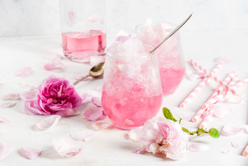 Fototapeta na wymiar Summer refreshing desserts. Vegan diet food. Ice cream frozen rose, froze, with rose petals and rose wine. On a white concrete table, with spoons, striped straws, petals and rose flowers. Copy space
